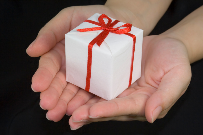two hands hold small white box wrapped with red ribbon