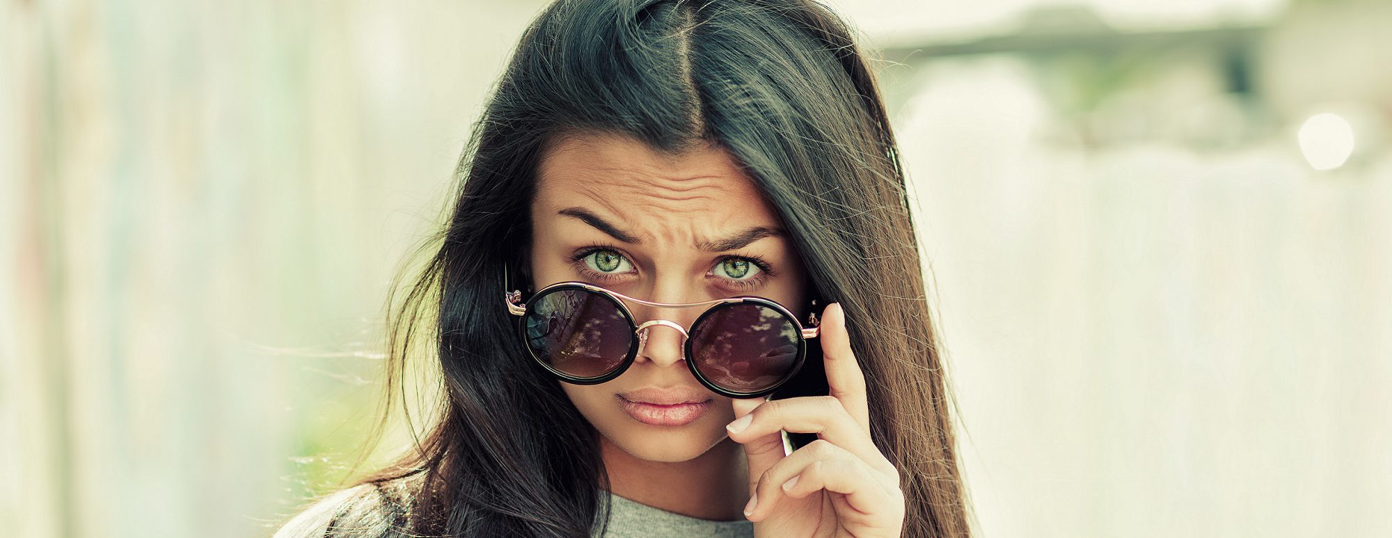 Closeup portrait beautiful young woman, lady looking at you camera over glasses gesture skeptically, isolated very green background. Negative human emotions, facial expression, feeling, body language