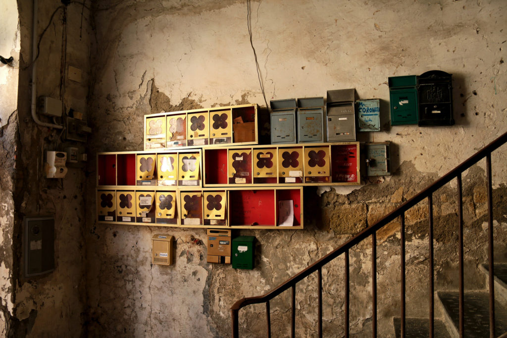tin mail boxes bunched together on a wall with a set of stairs by the side in an amber lit room